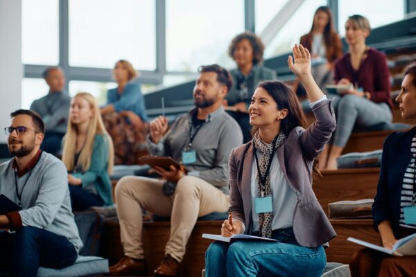 Female entrepreneur raising a hand to ask a question while attending business seminar.